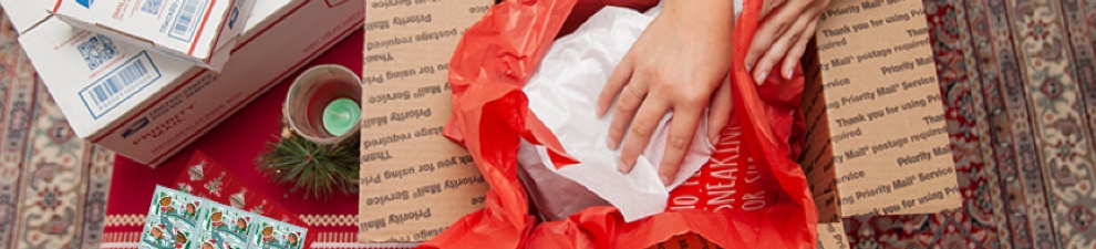 Young woman preparing holiday gifts and Priority Mail boxes to ship for December 25 delivery.